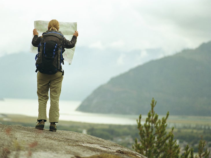 woman reading map while facing body of water