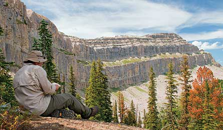 A hiker sits on the ground and overlooks the vast mountains and canyons of the Bob Marshall Wilderness. 
