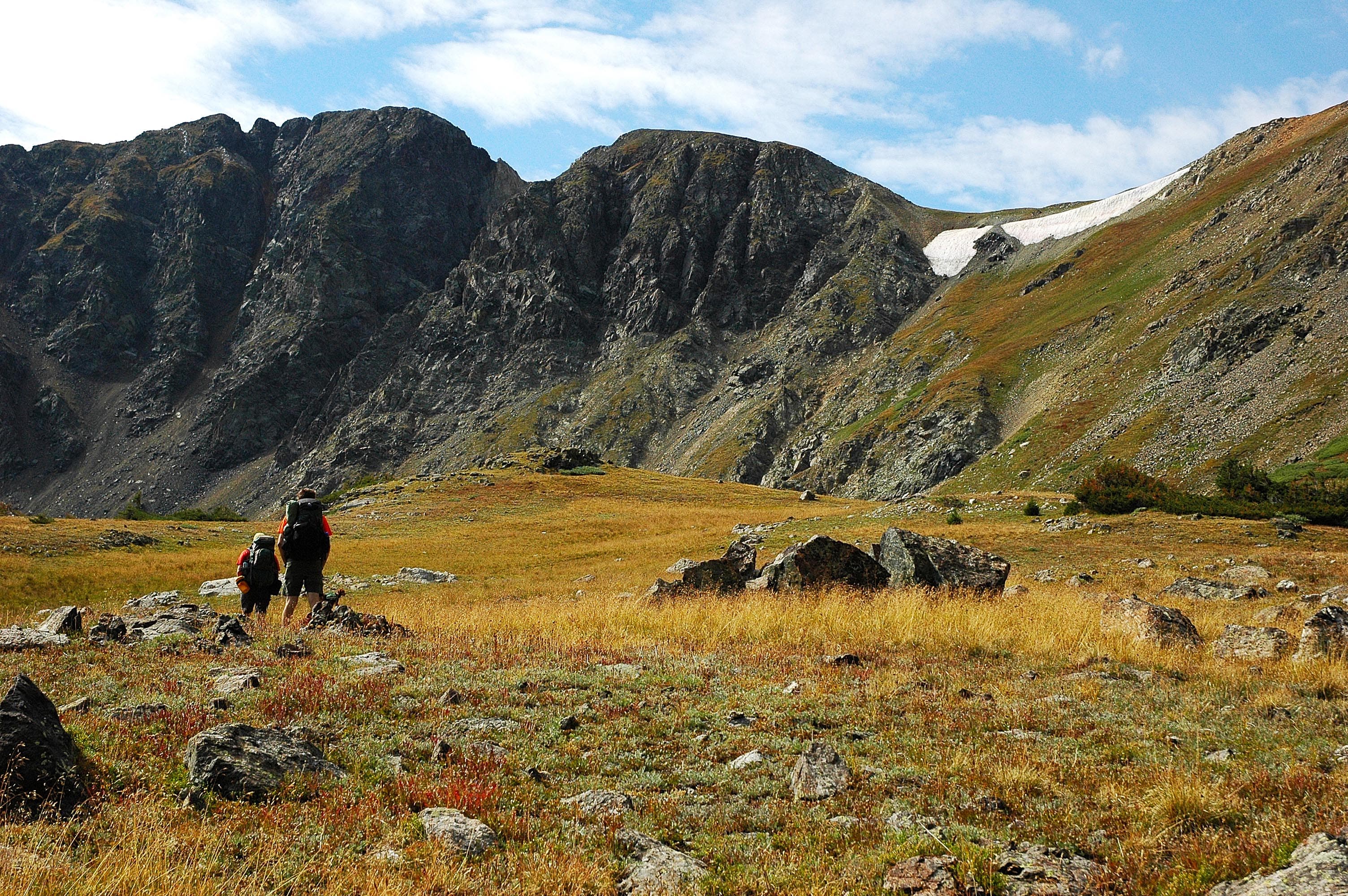 Two hikers walk across an open field just below the Continental Divide ridgeline. 