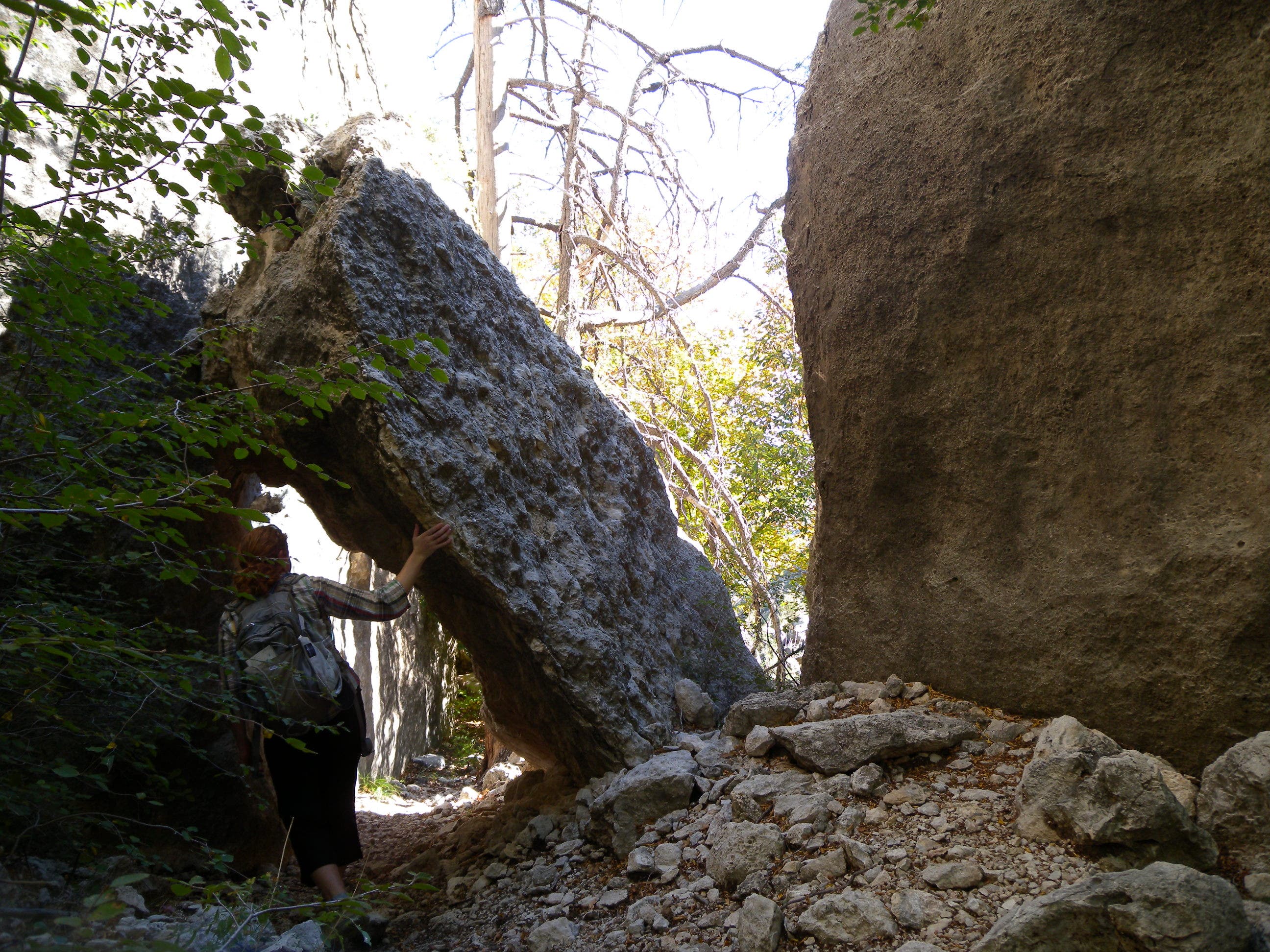 Boulders at the bottom of Bear Canyon on the second half of the Bowl Loop hike. Hiker walks in the shade beneath a large boulder at the bottom of Bear Canyon.