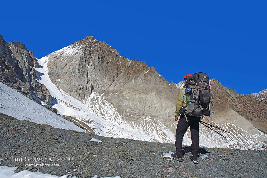 A hiker stands on the White Cloud Loop hike looking up at the snow-covered Castle Divide. 