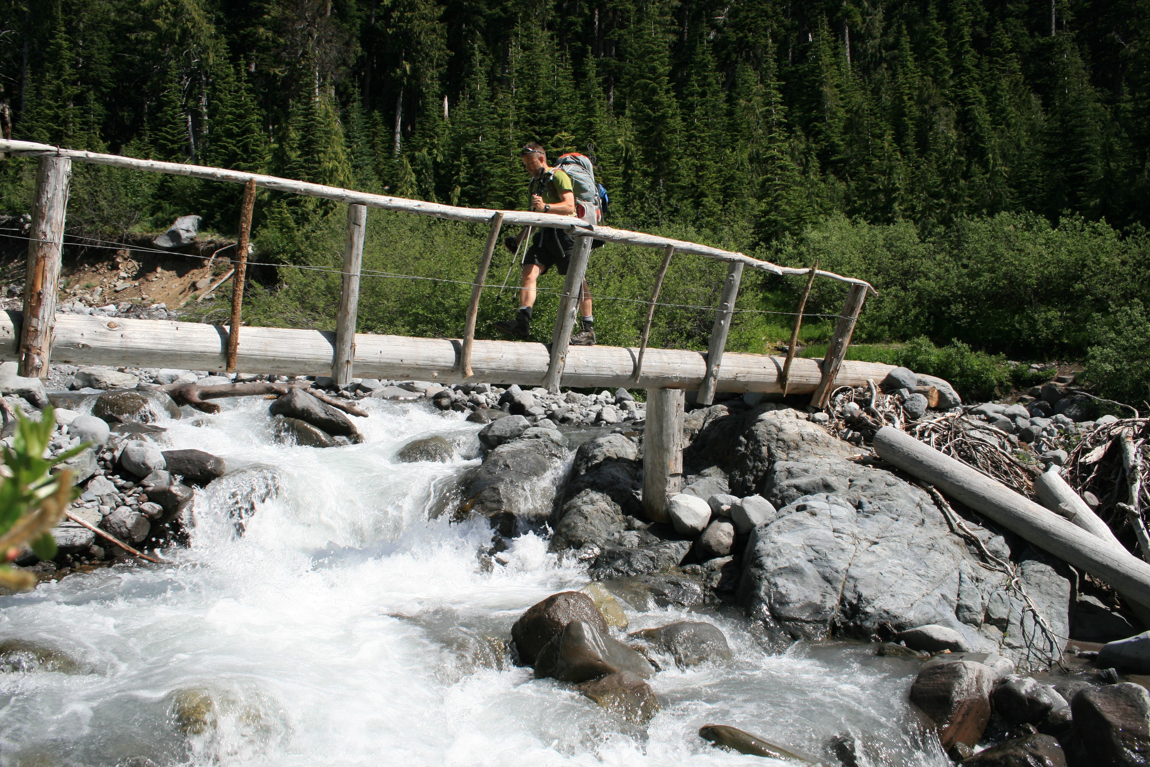 Crossing Fryingpan Creek on the way to Mowich Lake. Hiker crosses a log bridge over the rushing waters of Fryingpan Creek.