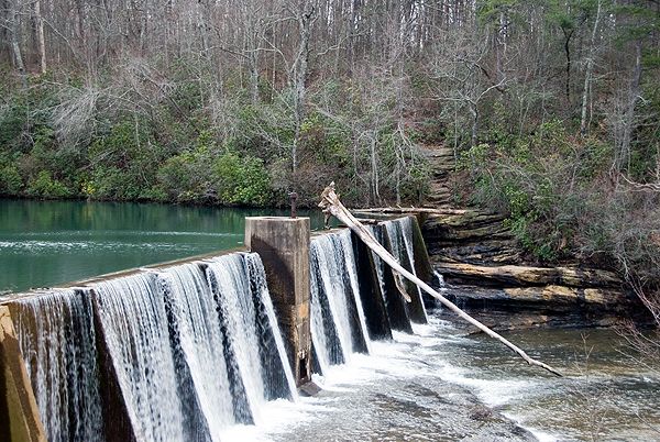 View of the dam at DeSoto Falls from the Picnic Area. The dam at Destoto Falls is a waterfall wider than it is tall with a fallen tree on it.