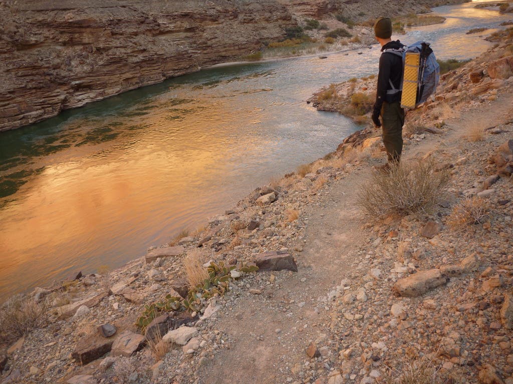 A hiker stands on the shores of Little Colorado River and catches the reflection of the early morning sun. 