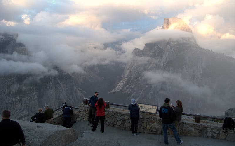 People gathered along a railed viewpoint looking at spectacular views of Half Dome.