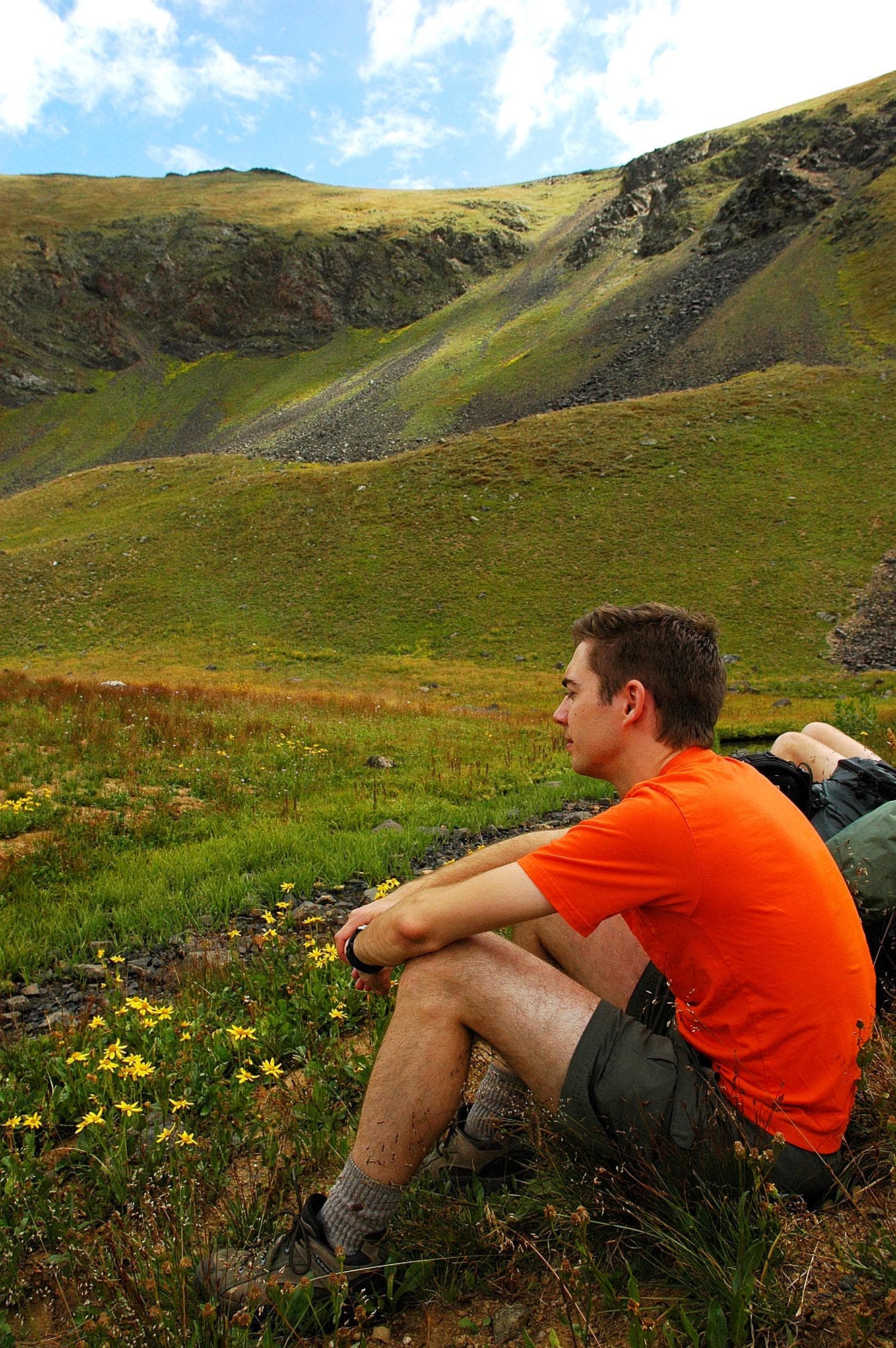 Hiker in an orange shirt sits on the side of the Continental Divide Trail partway along the Baker Gulch to Bowen Gulch loop trail. 