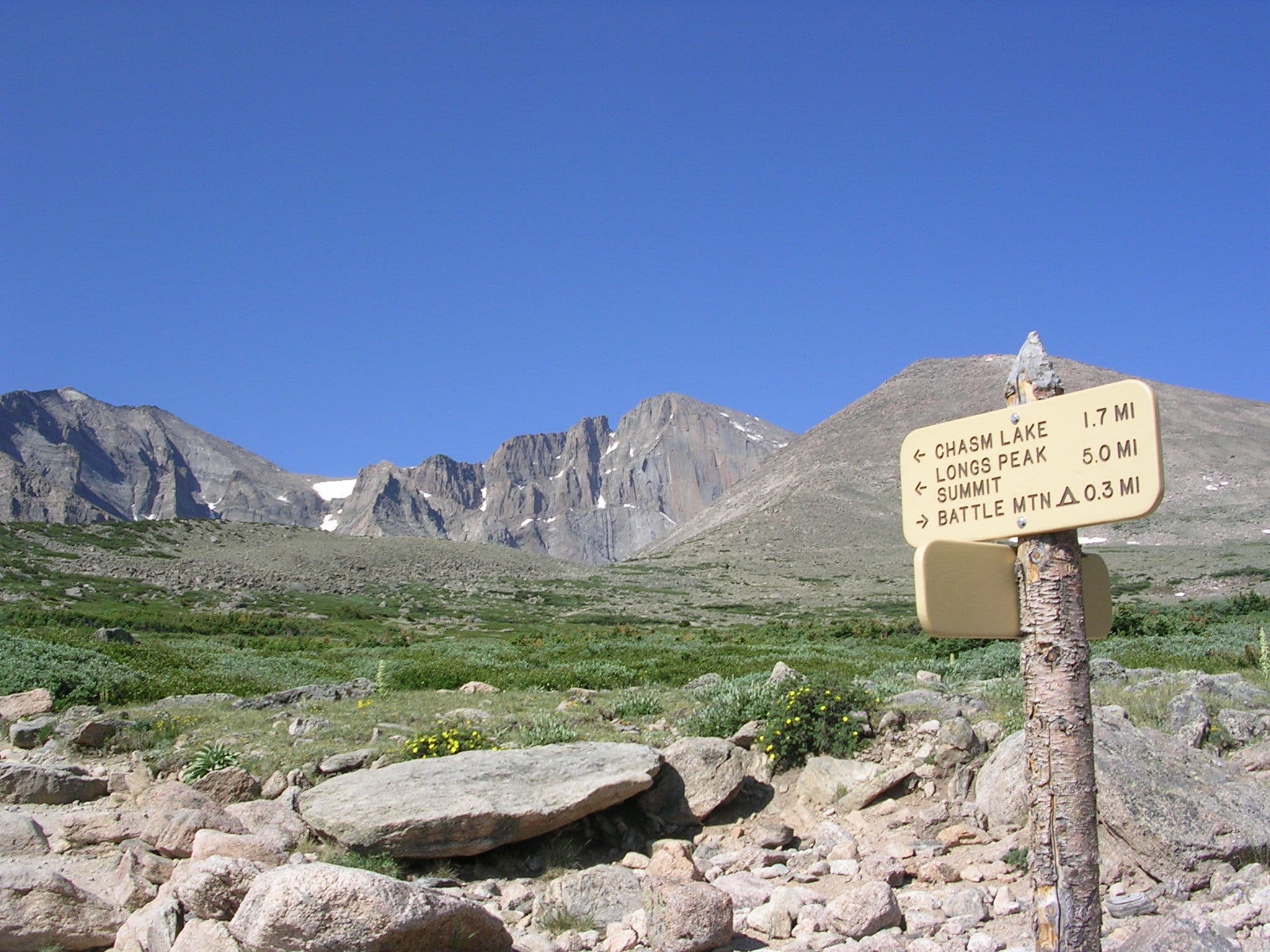 Chasm Lake trail sign with views of Longs Peak's Diamond Face behind it. 