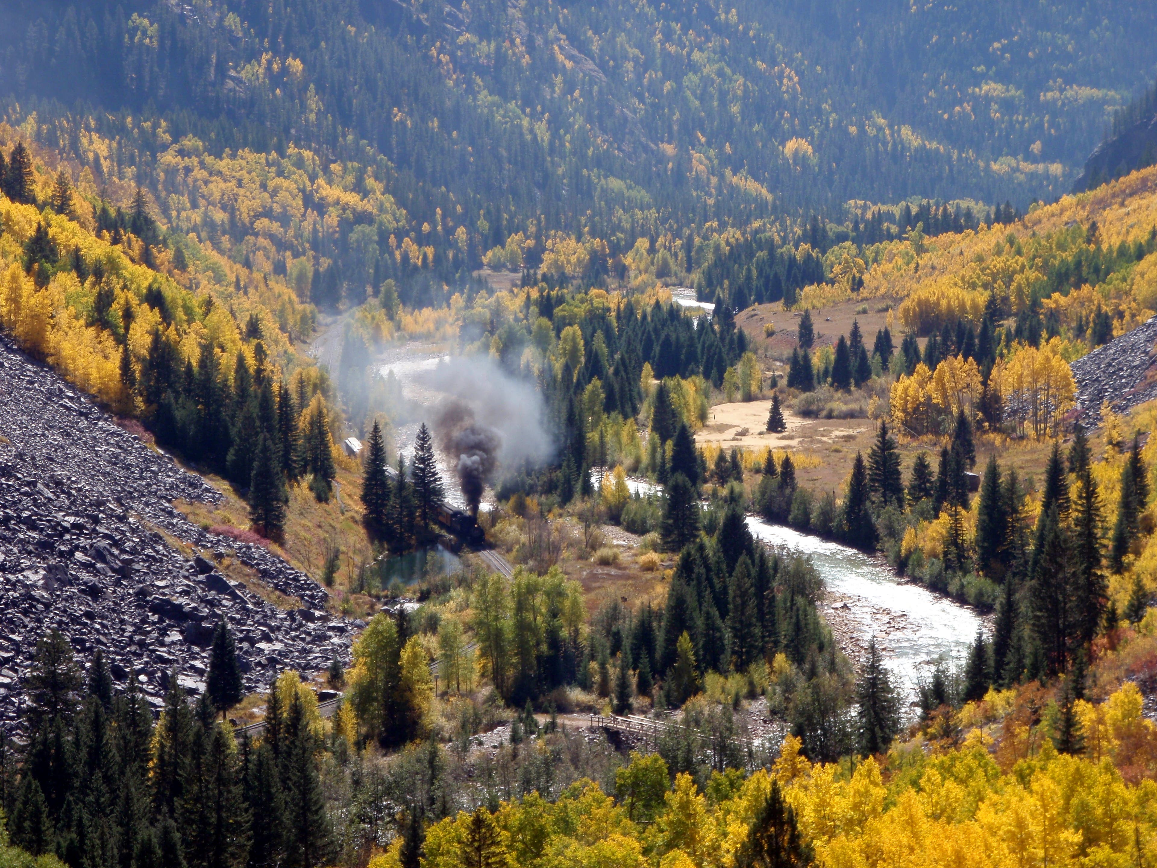 The Durango-Silverton Railway along the Colorado Trail. The Durango-Silverton train moving through the valley shooting black smoke above the bright yellow autumn trees.