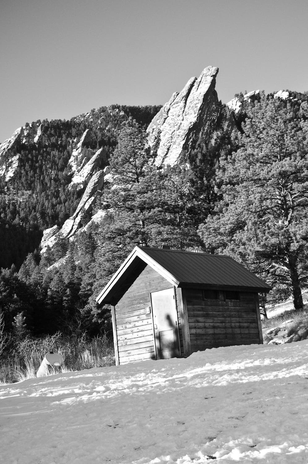 An outhouse sits at the top of Bluebell Road with the Flatirons in the background. 