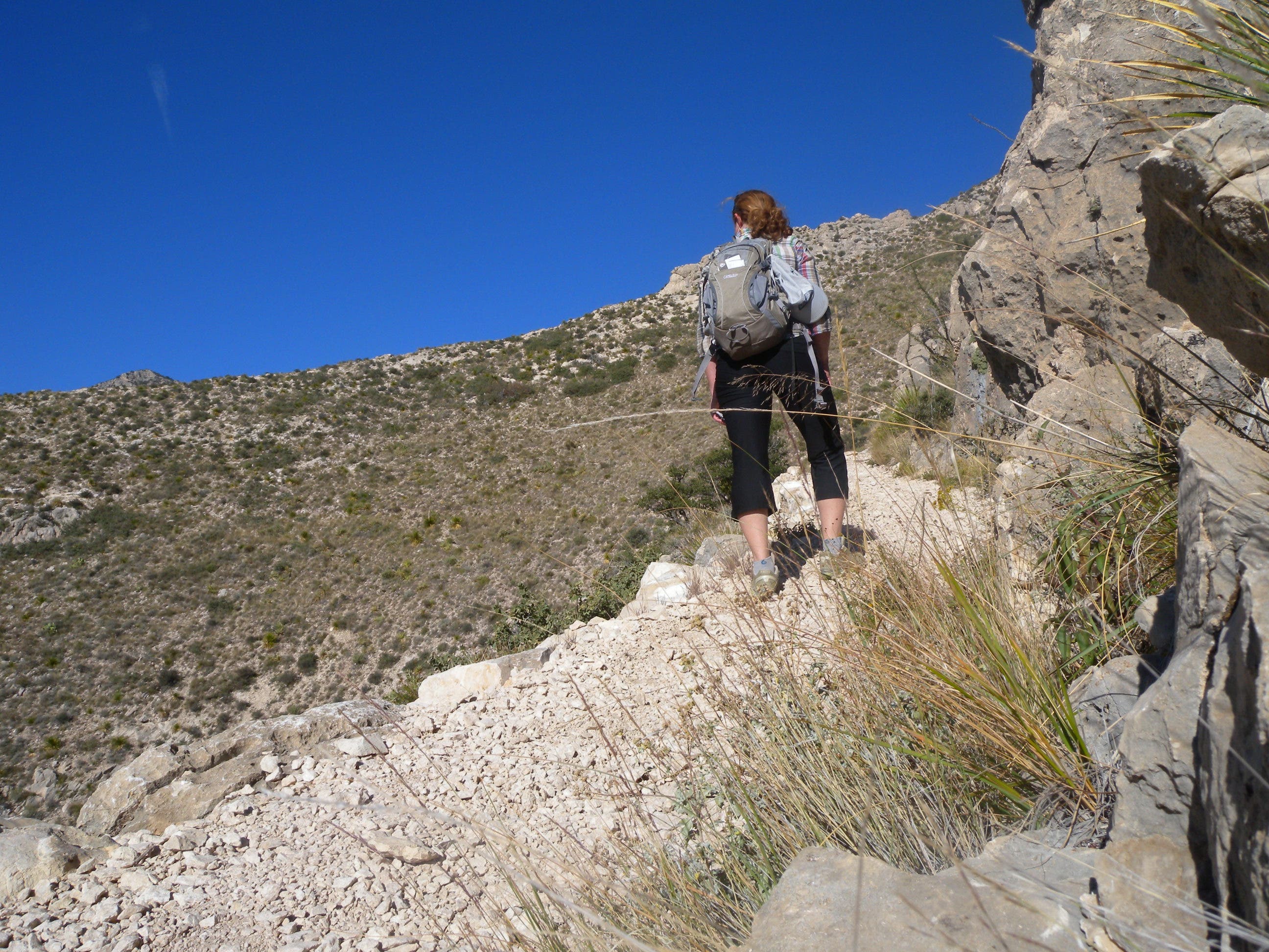 The first part of the Bowl Loop Trail is all uphill. Hiker stands on the rocky trail looking out at the mountains on a blue bird day.