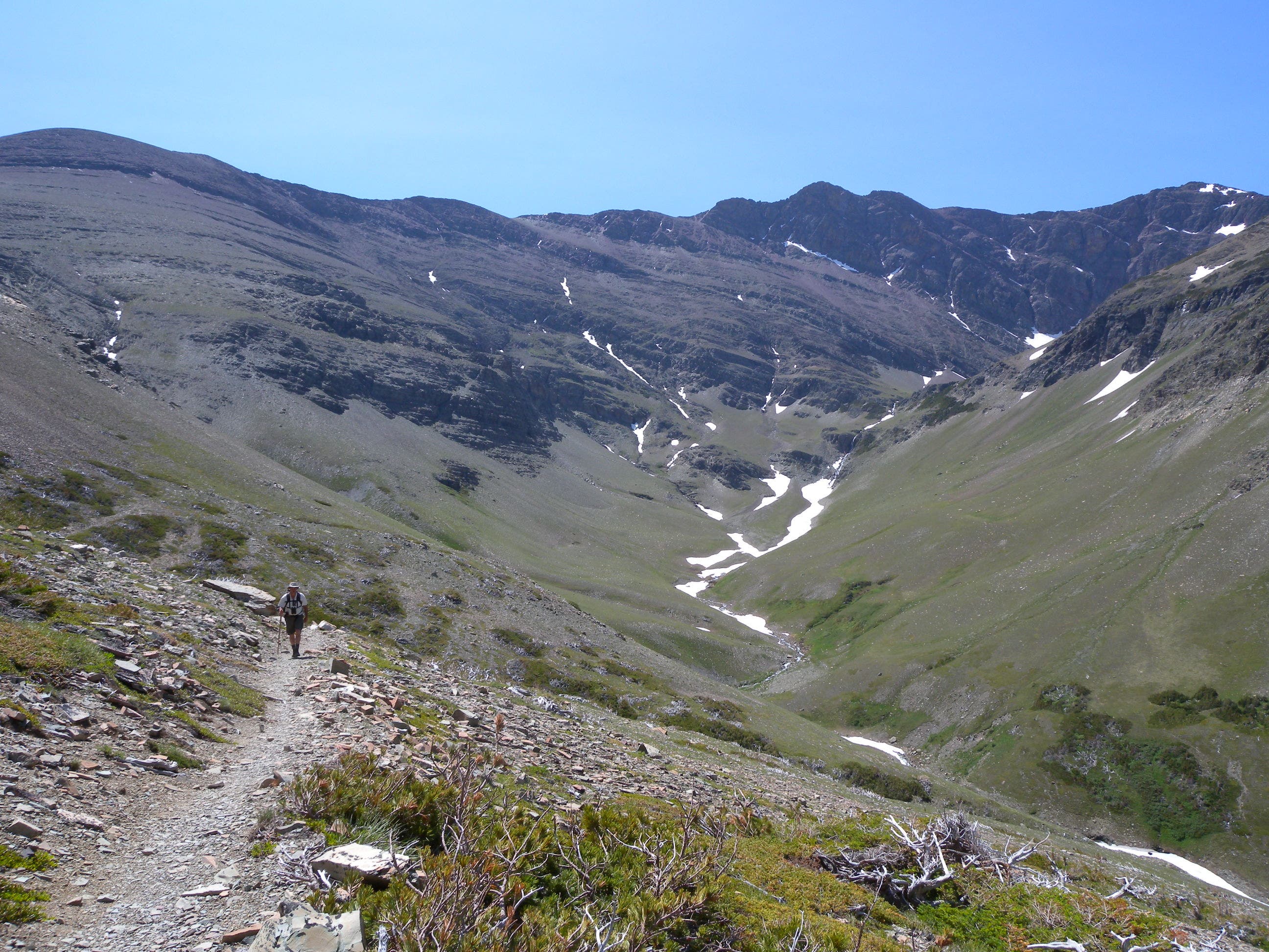 Heading into a valley before climbing a ridge into The Bowl. Hiker heading into a green valley with patches of snow.