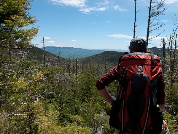 View from Bolton Mountain from Section 10 on the Long Trail. Hiker stands in a clearing atop Bolton Mountain looking out over views of the Green Mountains along the Long Trail Section 10 hike.