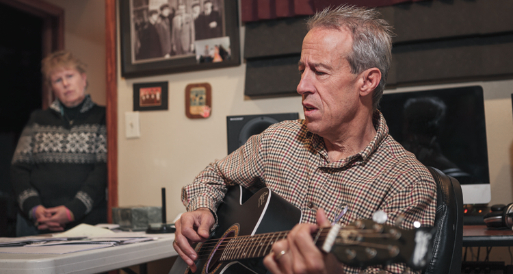 Paul Sacco playing the guitar while his wife, Connie, looks on (Heshphoto)