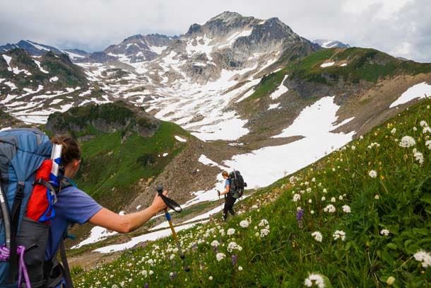 Climbing sisters Valerie (left) and Hayley Wall hike through a flowering alpine meadow above White Pass, enroute to Glacier Peak (still well out of…
