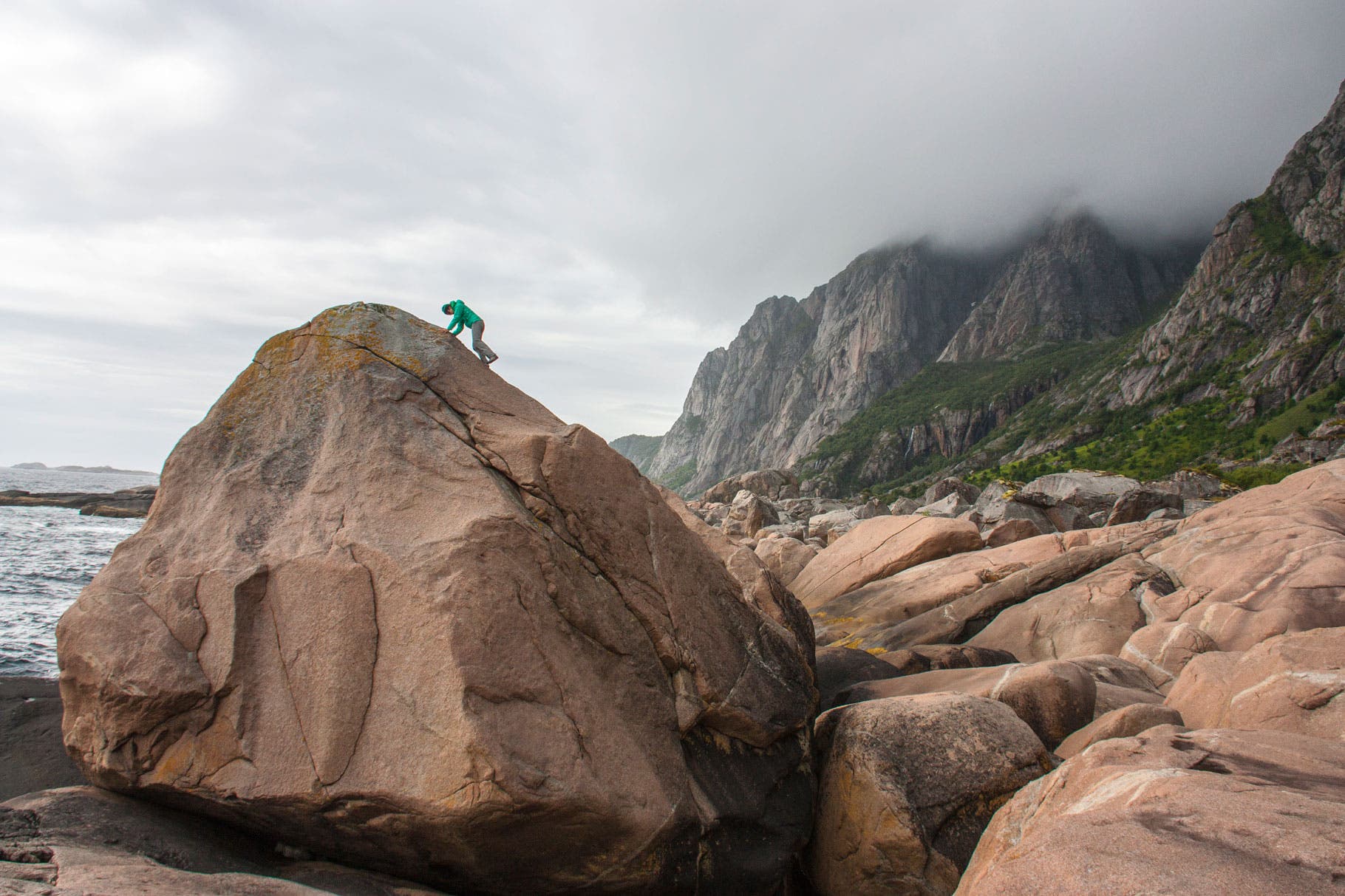 Majka Burhardt explores where the granite meets the ocean on the shore of Paradiset with the mountains leading to Henninsvaer behind.