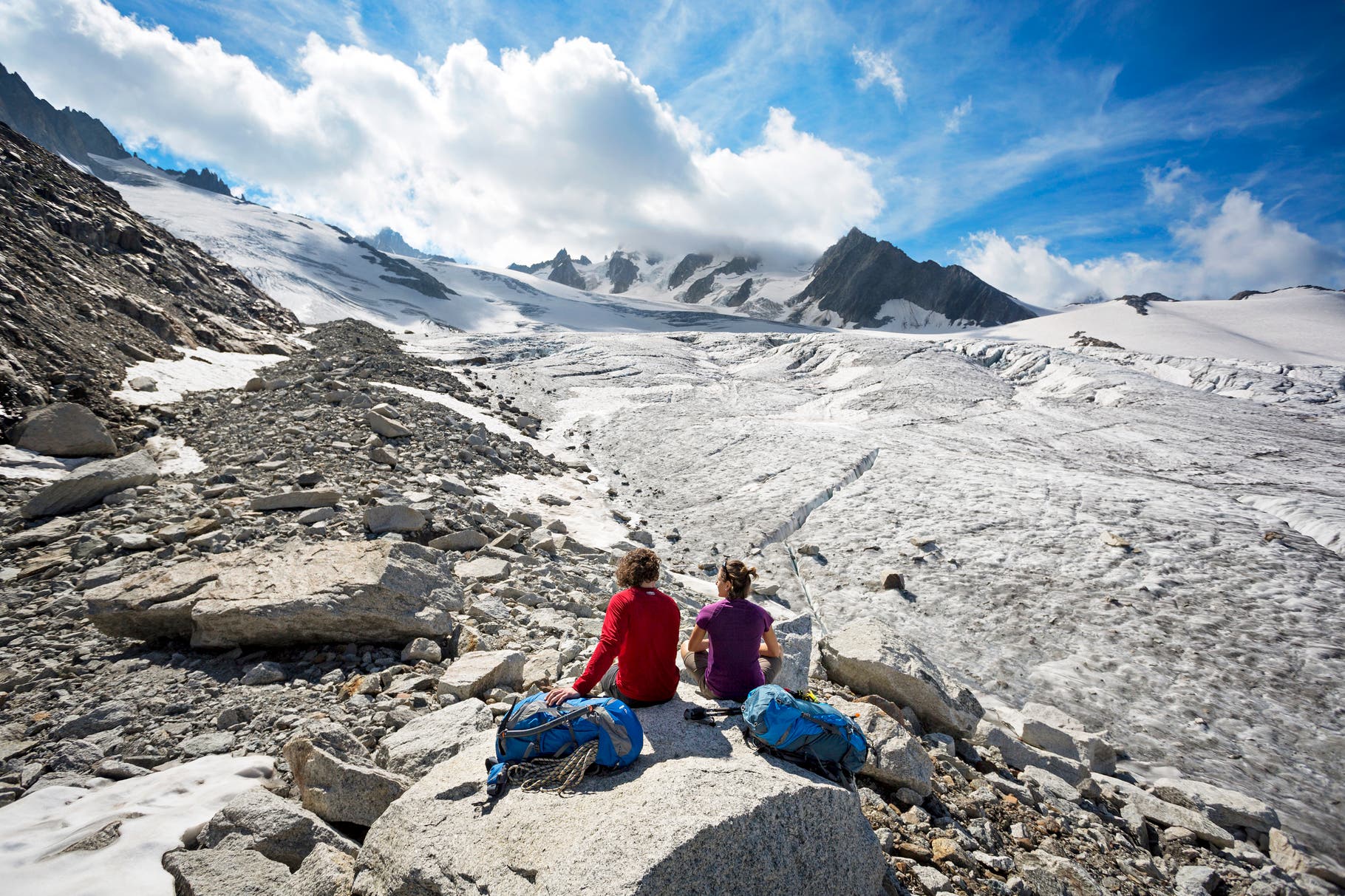 Two hikers sitting and taking a break on the edge of the Glacier du Tour on the first day of the Chamonix to Zermatt Glacier Haute Route.