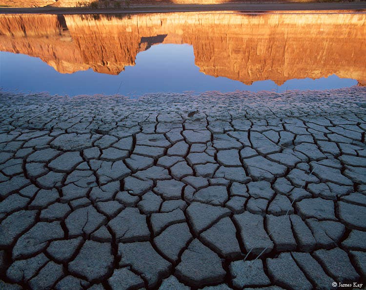 Morning sun illuminates the cliffs above drying mud at the foot of Lake Powell's abandoned Hite Marina boat ramp.