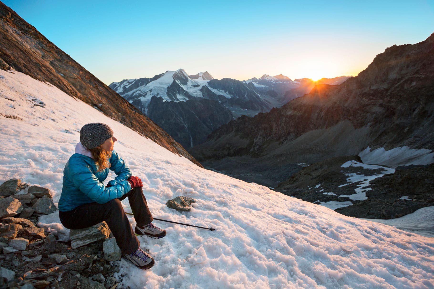 A woman sits in the Swiss Alps watching the sunset on a summer day during a hiking tour of the Chamonix to Zermatt Glacier Haute Route.