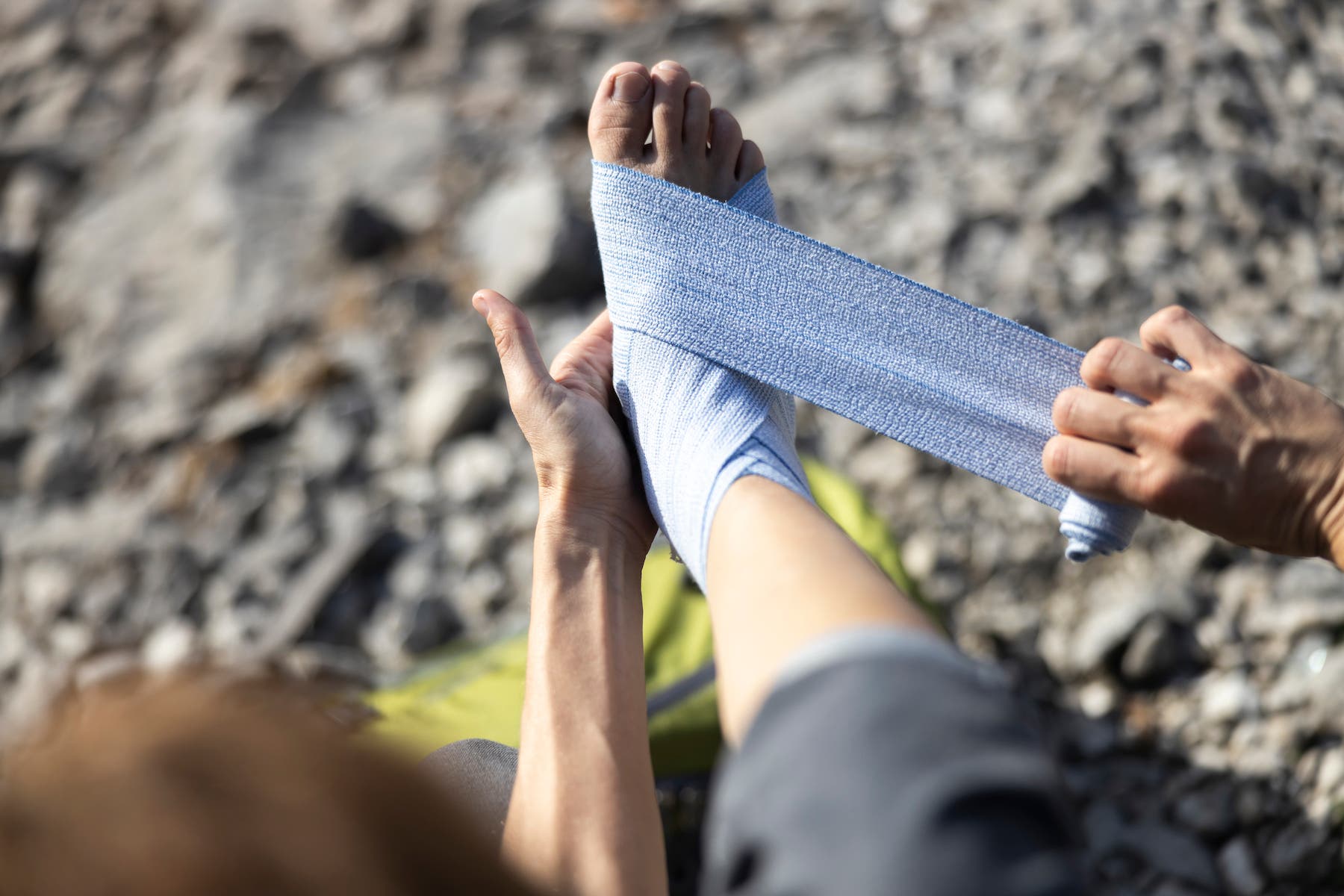 Personal Perspective of Adult Woman Wrapping Elastic Bandage Around Her Sprained Ankle in Nature