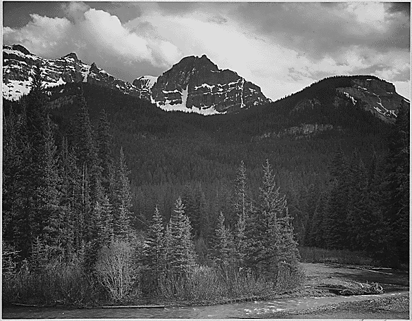 Stream in foreground, with view of tress and snow on mountains. “Mountain-Northeast Portion, Yellowstone National Park,” Wyoming, 1933-1942 photo: Ansel Adams / U.S. Department of the Interior