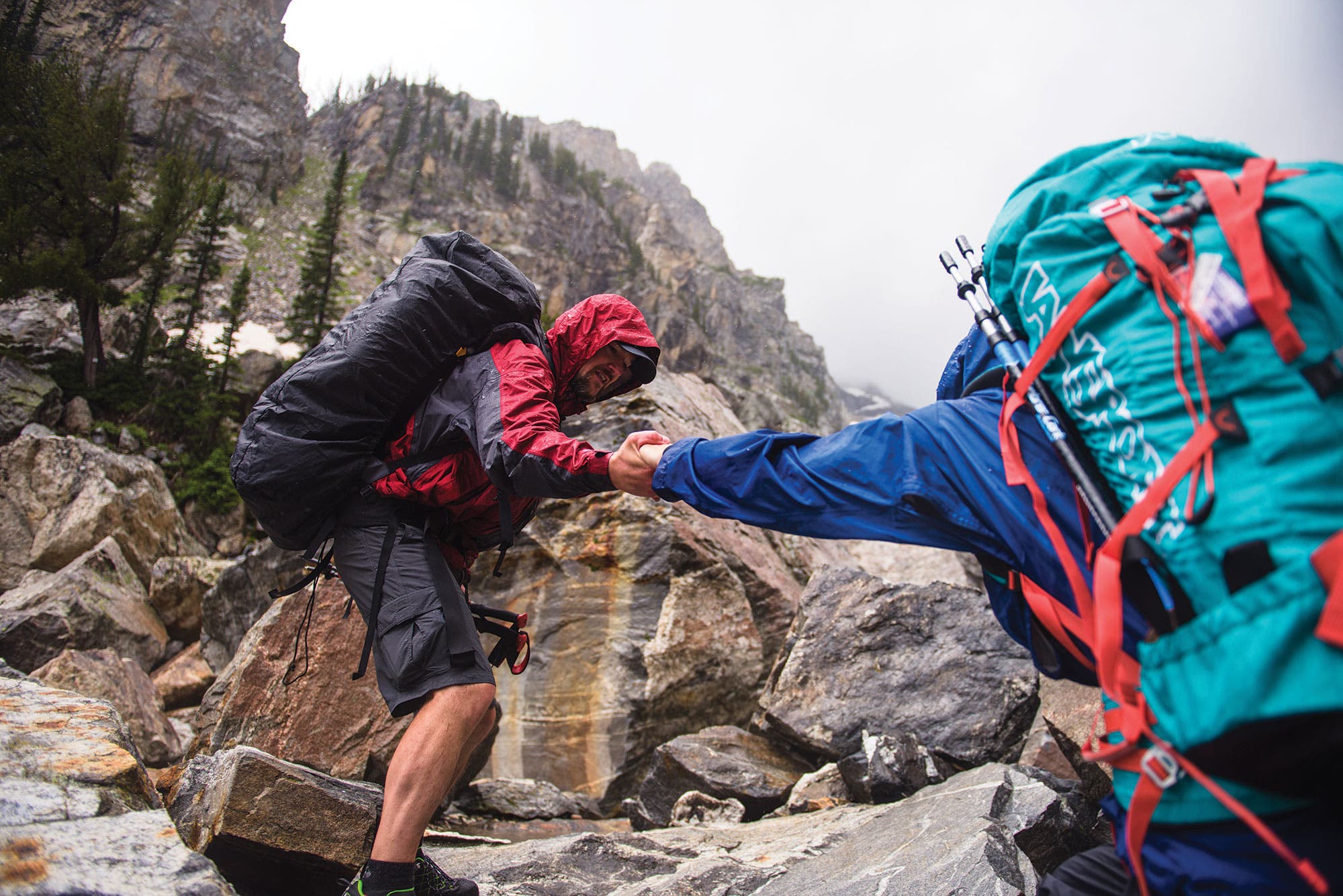 One hiker gives another a hand for support on a rainy Grand Teton hike through a boulder field. 