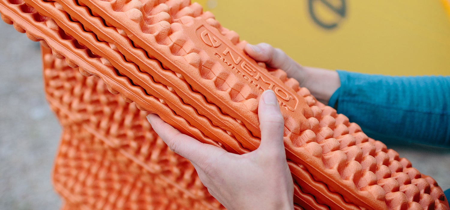 "Person's hands folding up an orange Nemo Switchback sleeping pad."