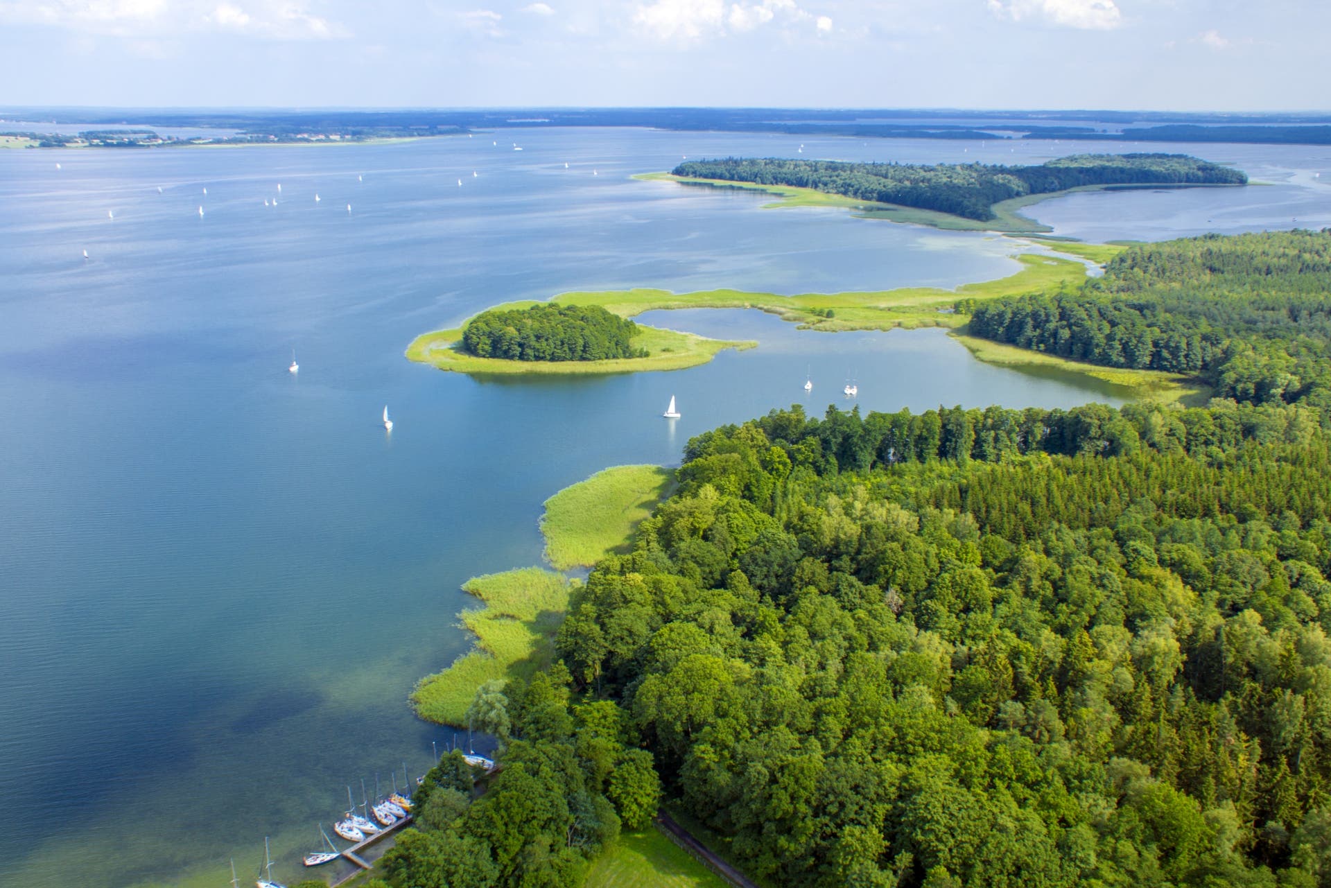 Water sweeps the landscape surrounded by trees and small islands in Poland's Lake District.