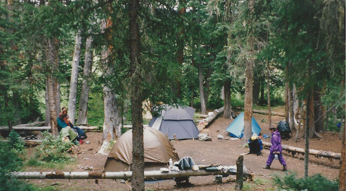 97 Boulder Lake Campsite_cropped Three tents sit between logs at a campsite in Boulder Lake, Colorado. A woman in all purple walks toward the tents.