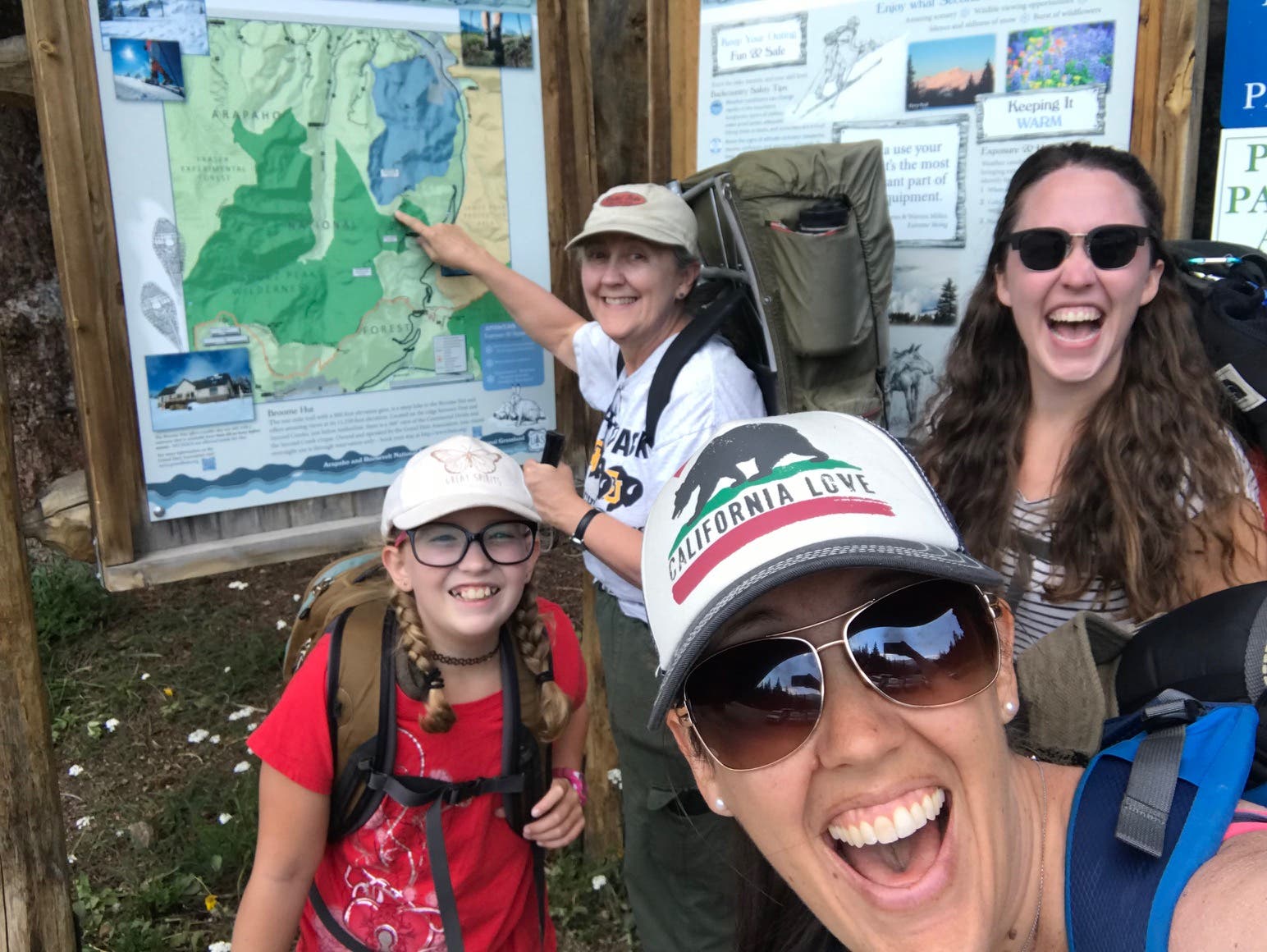 Three generations of women stand in front of the trail sign smiling with joy as they celebrate the beginning of their trip.