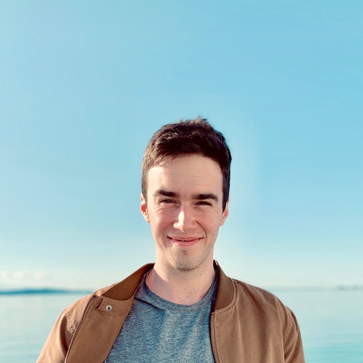 Dave bonan-headshot Dave Bonan smiles at the camera in a brown leather jacket with a clear blue sky and body of water in the background.