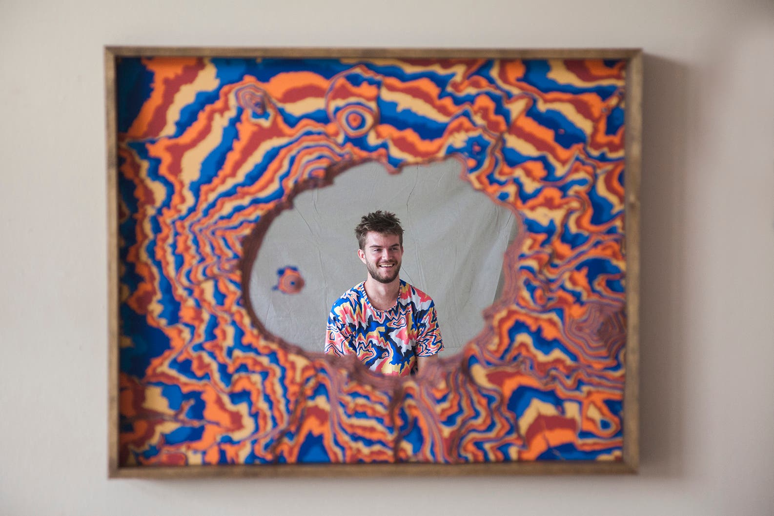 Chris Warren looks in the mirror with a topographic design surrounding it. He is a white man with short brown hair and a beard