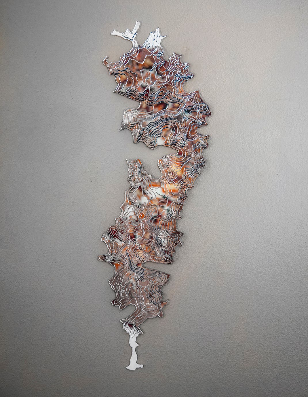 Fire+Reflection+web Mirror topographic sculpture hangs on a gray wall.