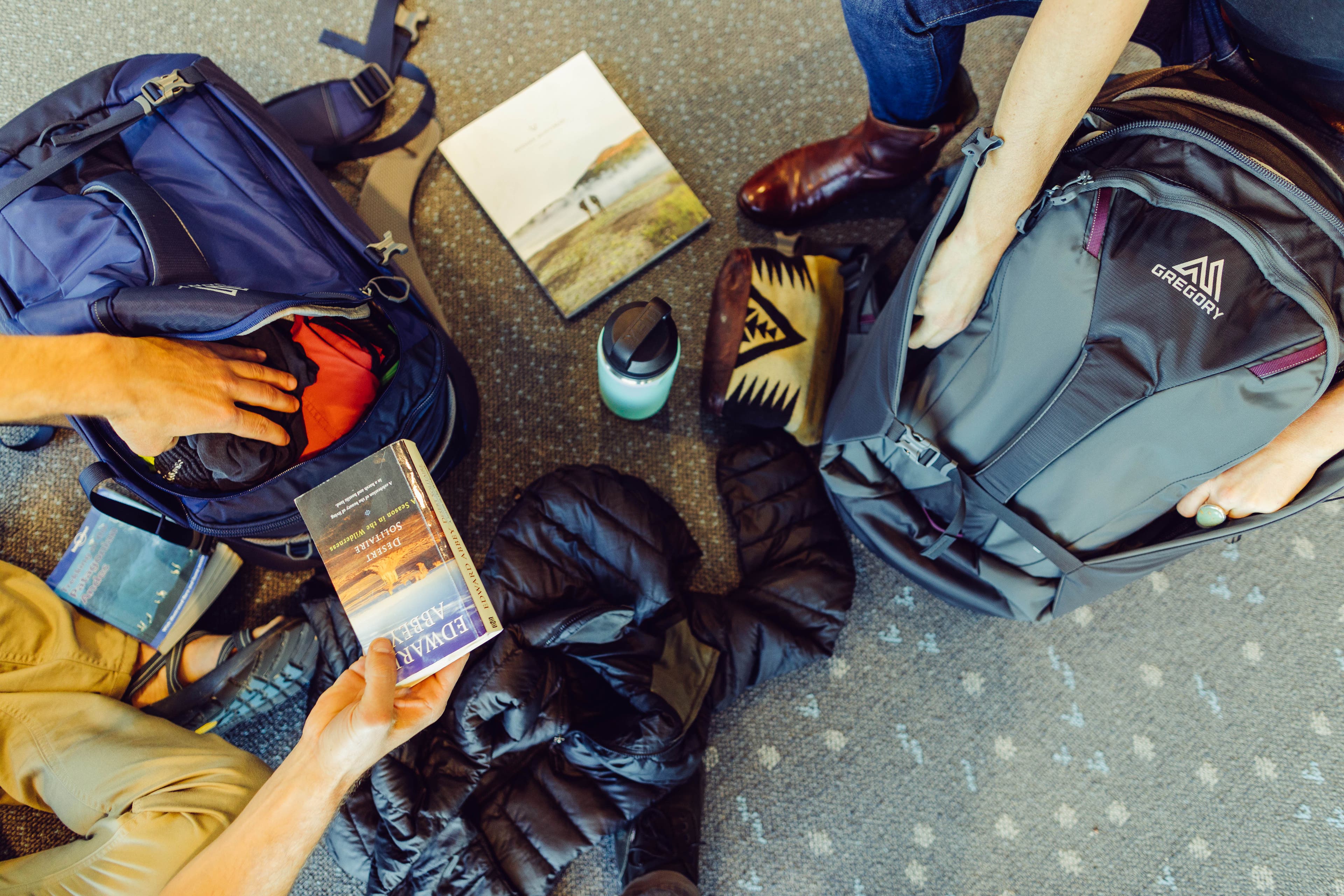 GMP_F18_PraxusProxy11 Two people put things away in their Gregory backpacks on an airport floor.