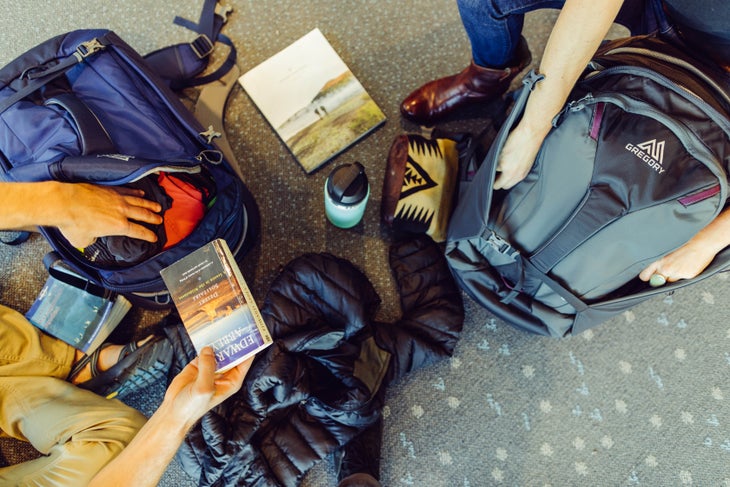 GMP_F18_PraxusProxy11 Two people put things away in their Gregory backpacks on an airport floor.