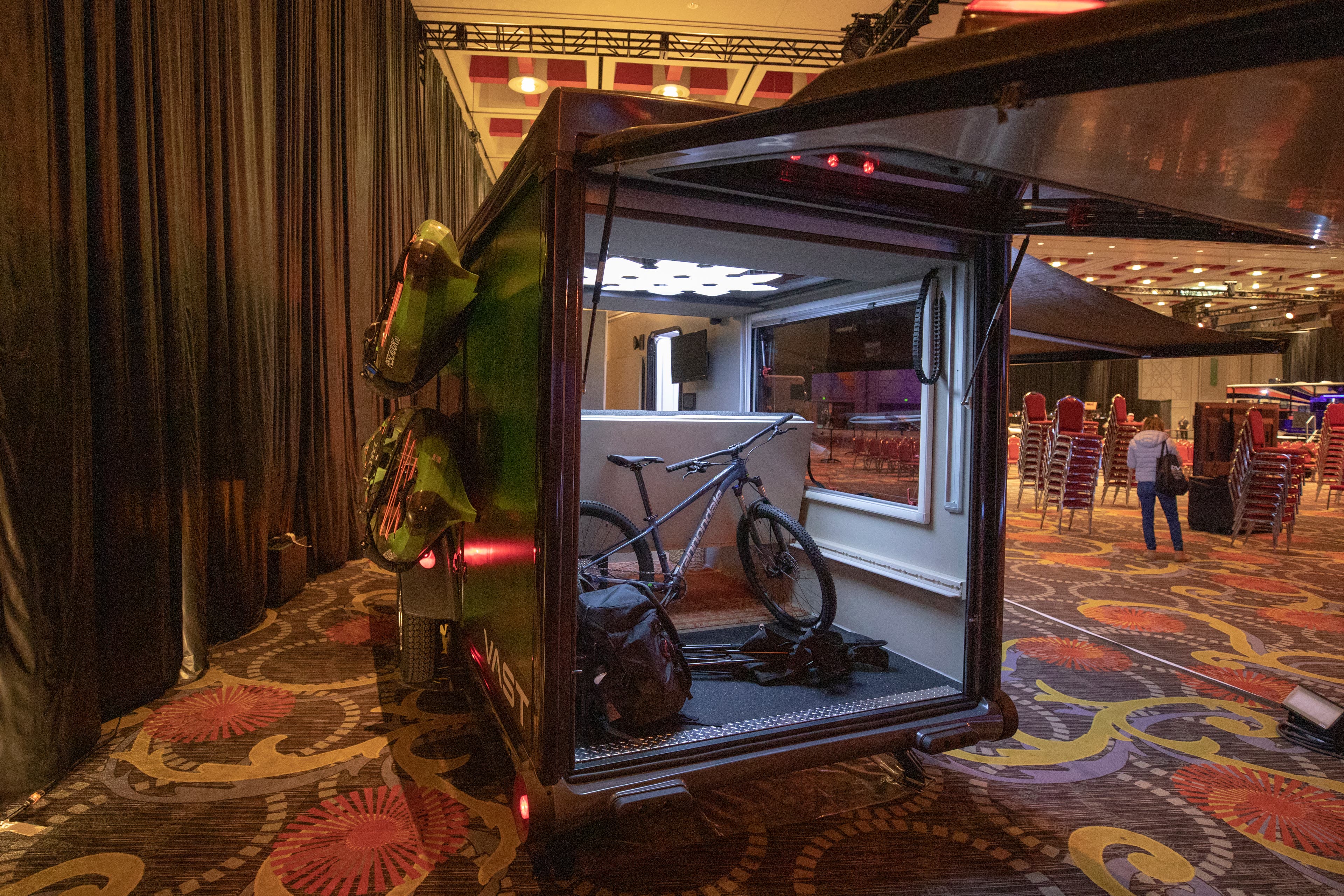 view of the SylvanSport VAST RV from the back. Two kayaks are attached to the side and the back is open showing a bike, camp chair, and backpack in…