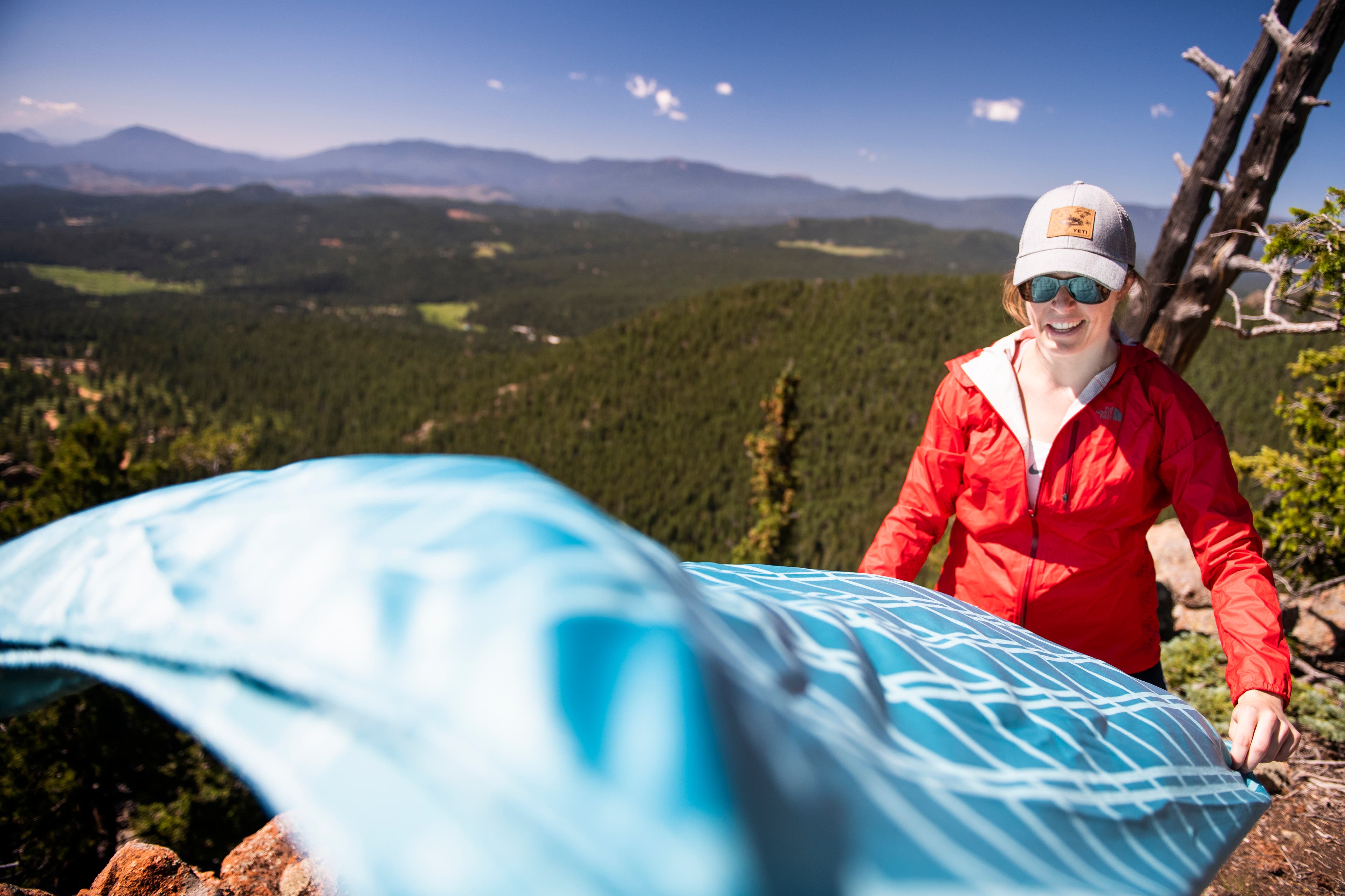20190710_ViewRanger_053 White woman in red jacket fluffs teal tablecloth on the side of a cliff.