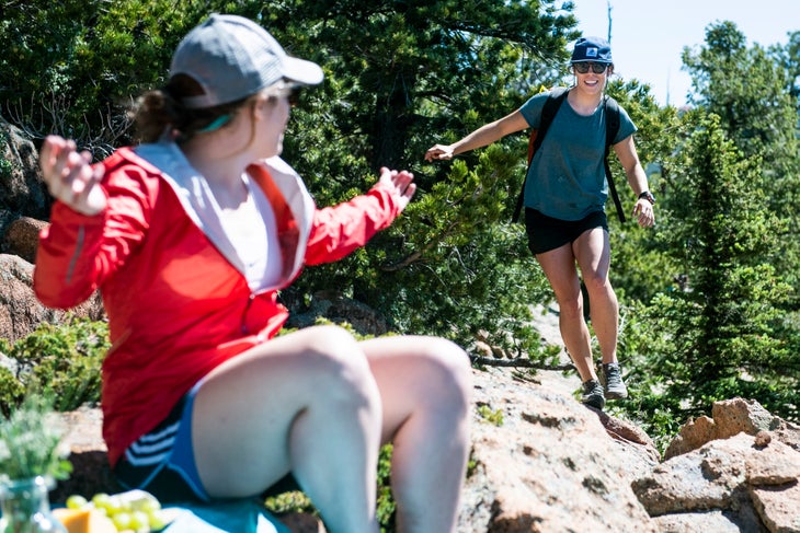 20190710_ViewRanger_148 White woman in muted blue shirt walks along edge of rocks toward another white woman in a red jacket sitting down on the rocks.
