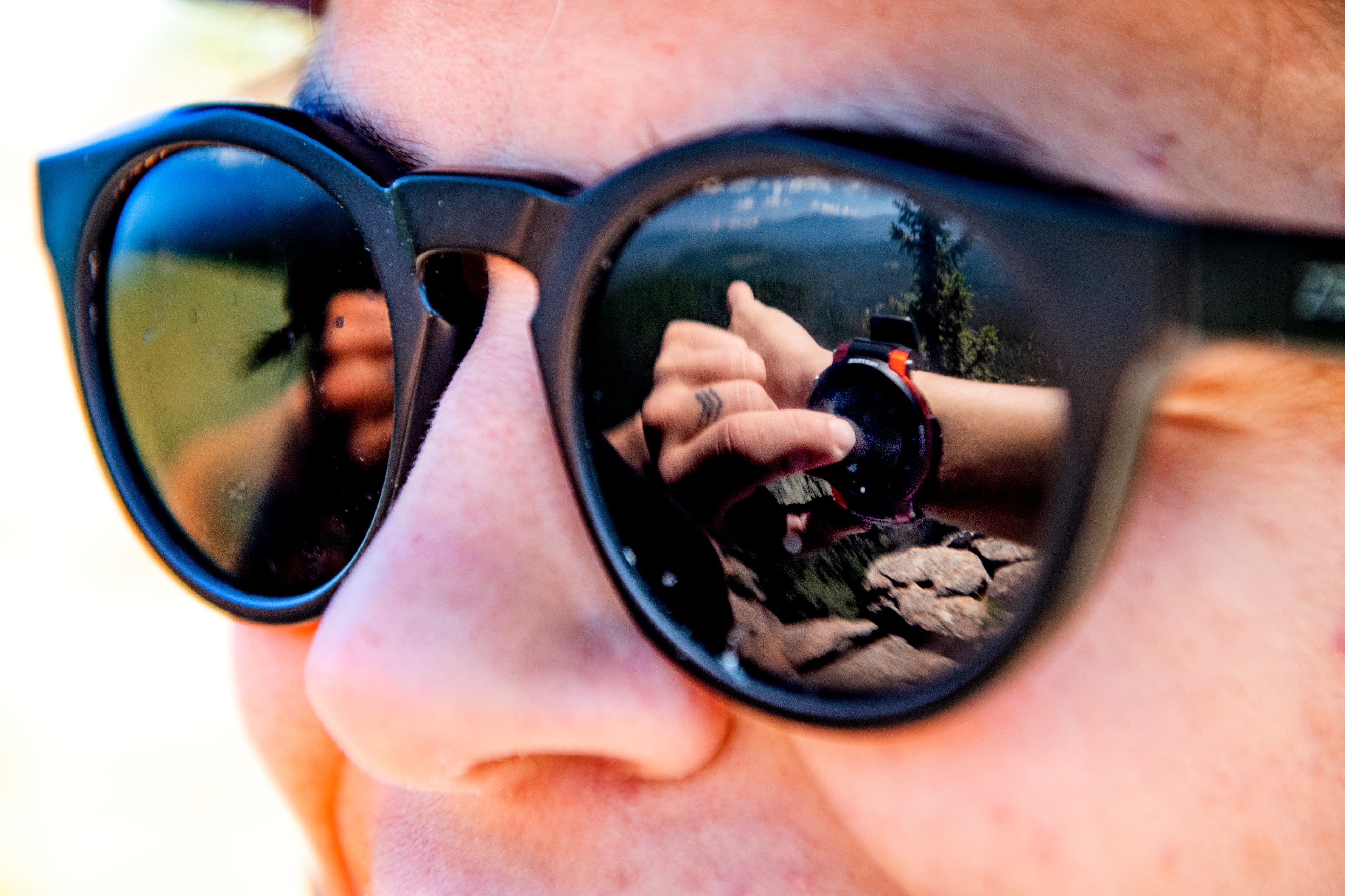 Close up shot of black sunglasses reflecting a mountainscape with a Casio watch on a wrist in the foreground of the reflection.