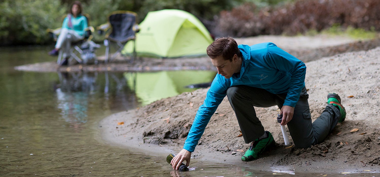 "White man in blue jacket refills water bottle with Lifestraw bottle cap in his hand."