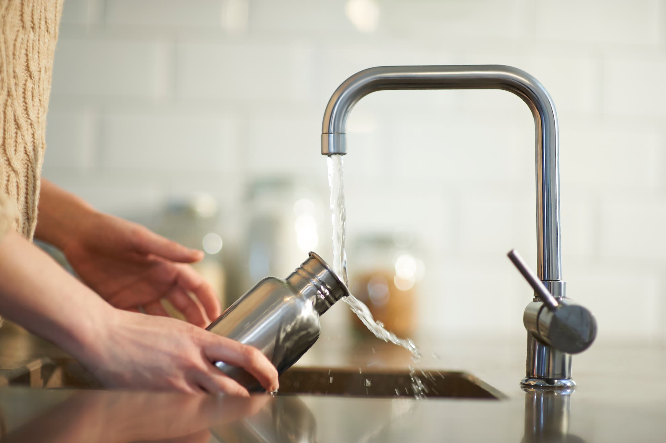A woman washes a steel water bottle in a kitchen sink.