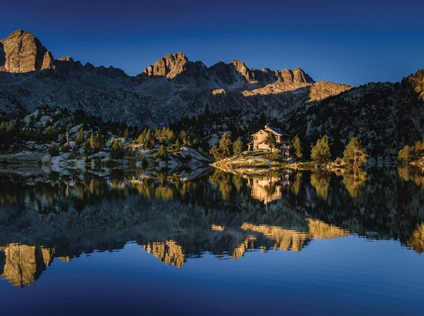 View of a lake reflecting rocky mountains on the Carriages of Fire (Carros de Foc) trail.