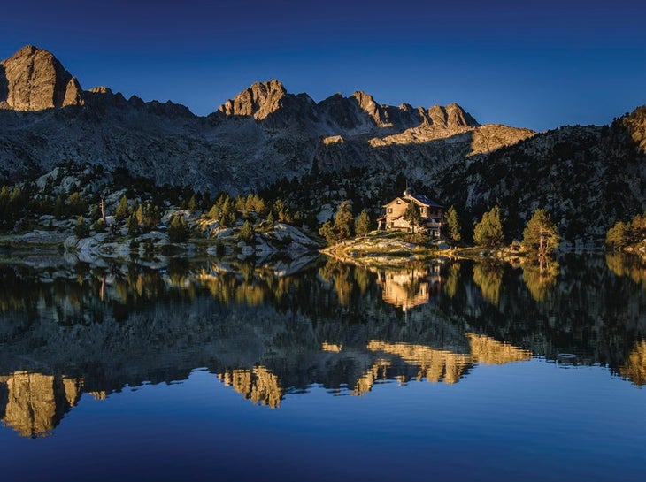 Carros de Foc_Estany Llong Shelter@CTB_Sergi Boixader View of a lake reflecting rocky mountains on the Carriages of Fire (Carros de Foc) trail.