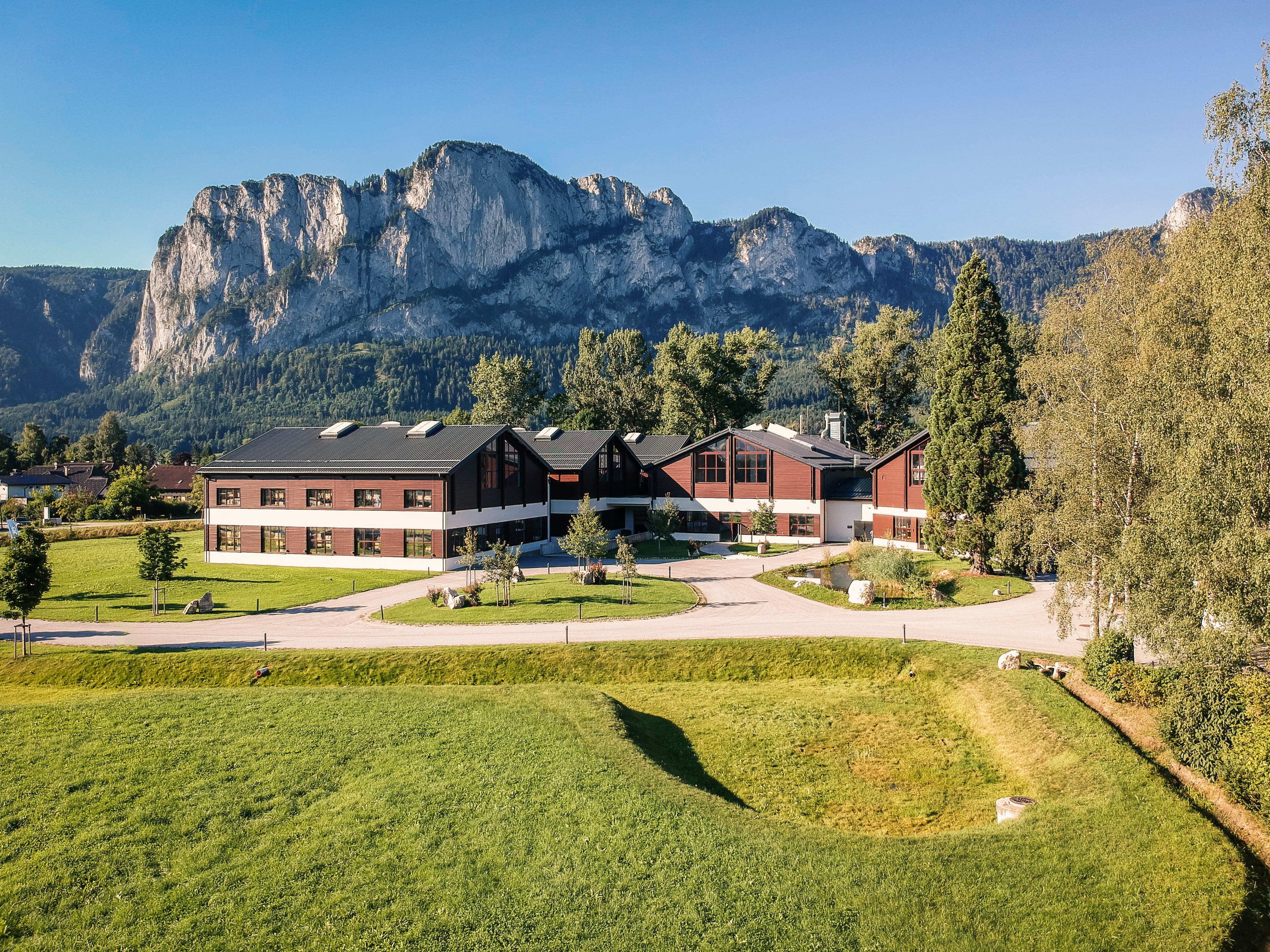Firma_Komperdell_016 Komperdell's headquarters is a red brick building sitting with grass in the foreground and a rocky cliff behind it. Clear blue skies above in…