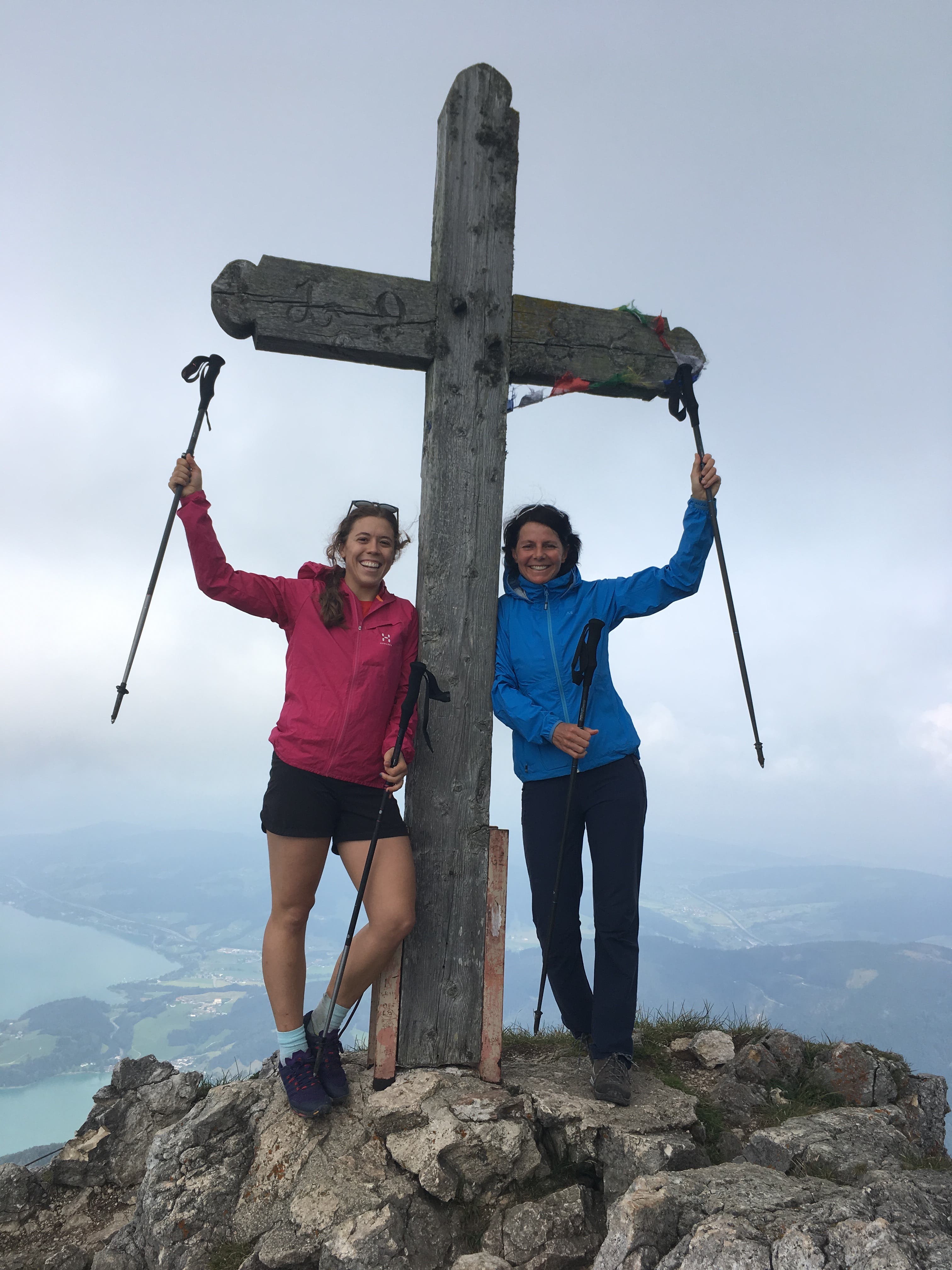 Emma Murray and Gerlinde Kaltenbrunner, two white women stand near a cross at the summit of Schafburg, Austria.