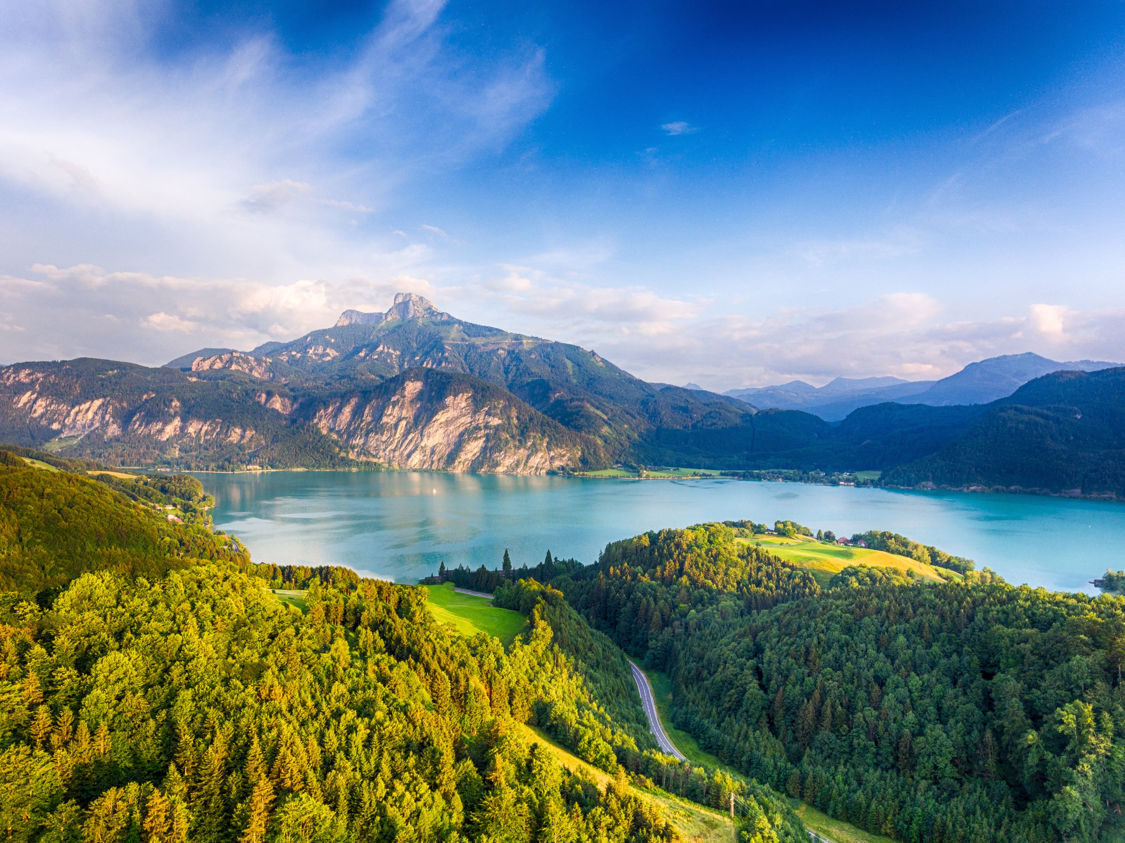 iStock-978552706 Austrian hills covered in evergreen trees surrounding a turquoise lake with rocky mountains in the background.