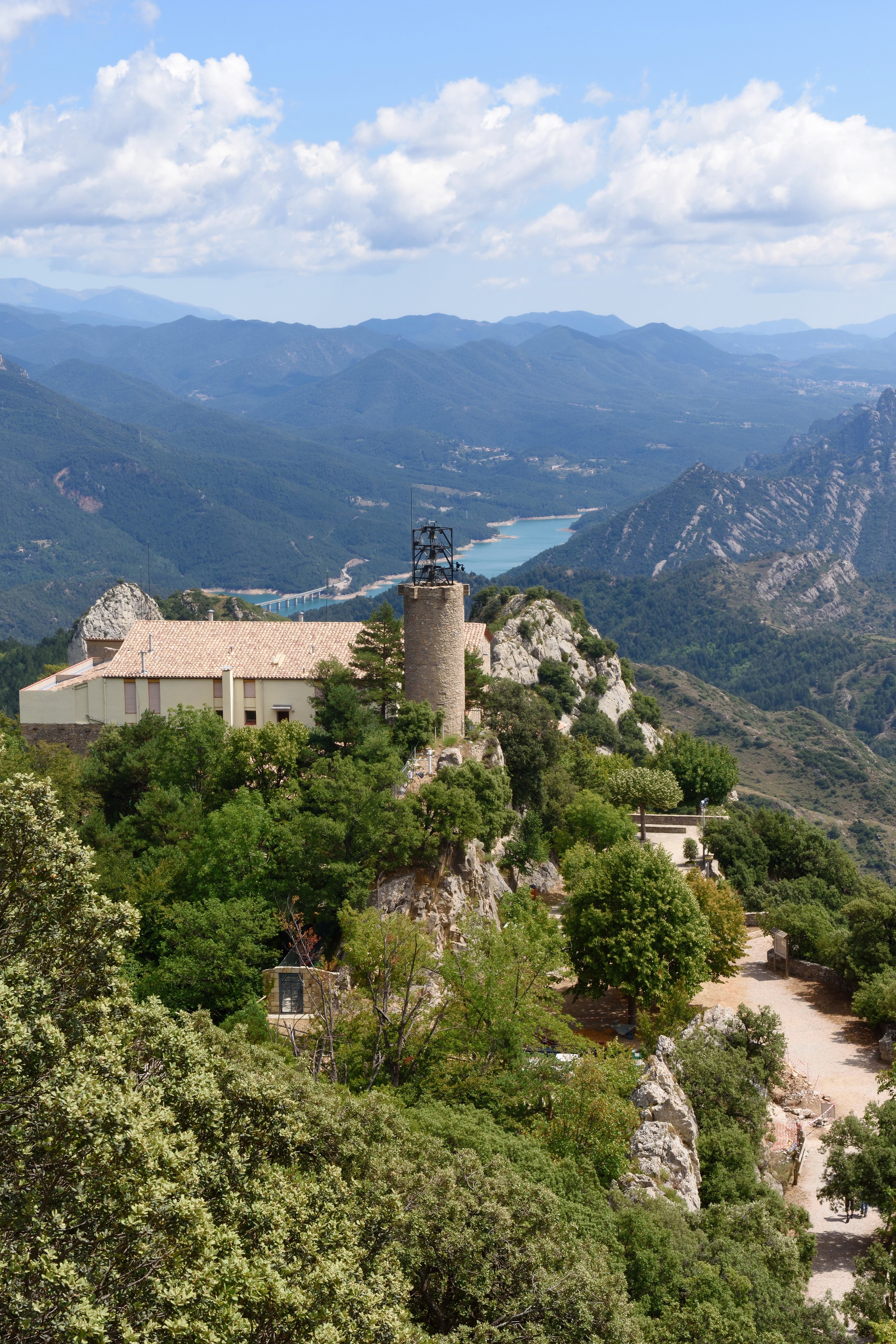 Queralt Sanctuary, a stone building, sits on a hill with the mountains and aqua river of the Cami des Bon Homes trail in Catalonia.