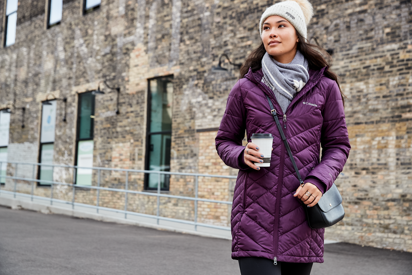 Women in purple Columbia jacket holding coffee in the street.