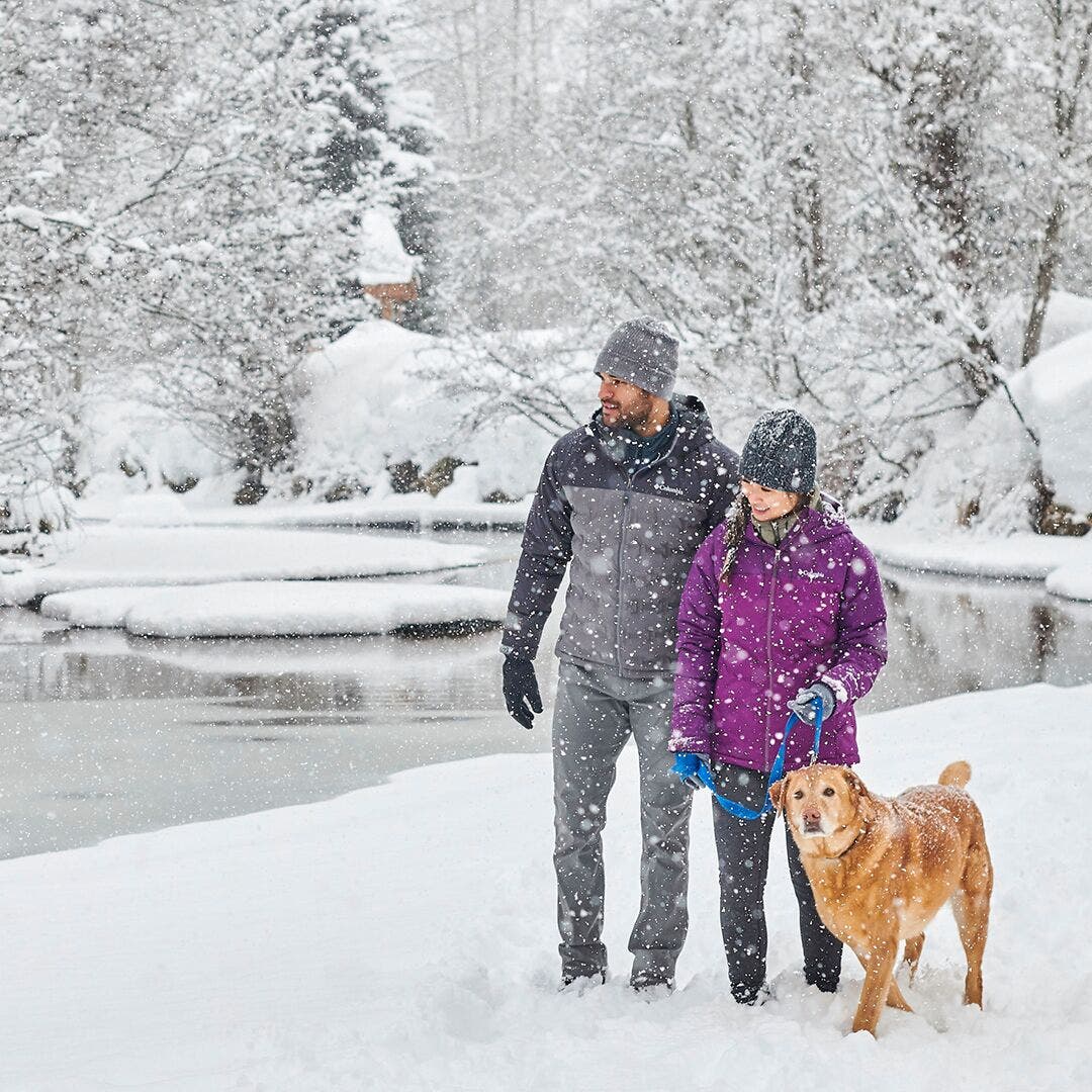 dickys columbia Man and women in Columbia jackets walking along creek in winter with their dog.
