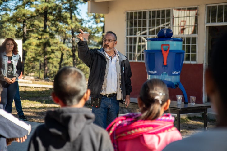 DSC09526 Department of Health official from Chihuahua holds up a glass of clear filtered water at the front of the presentation space in the courtyard by the…
