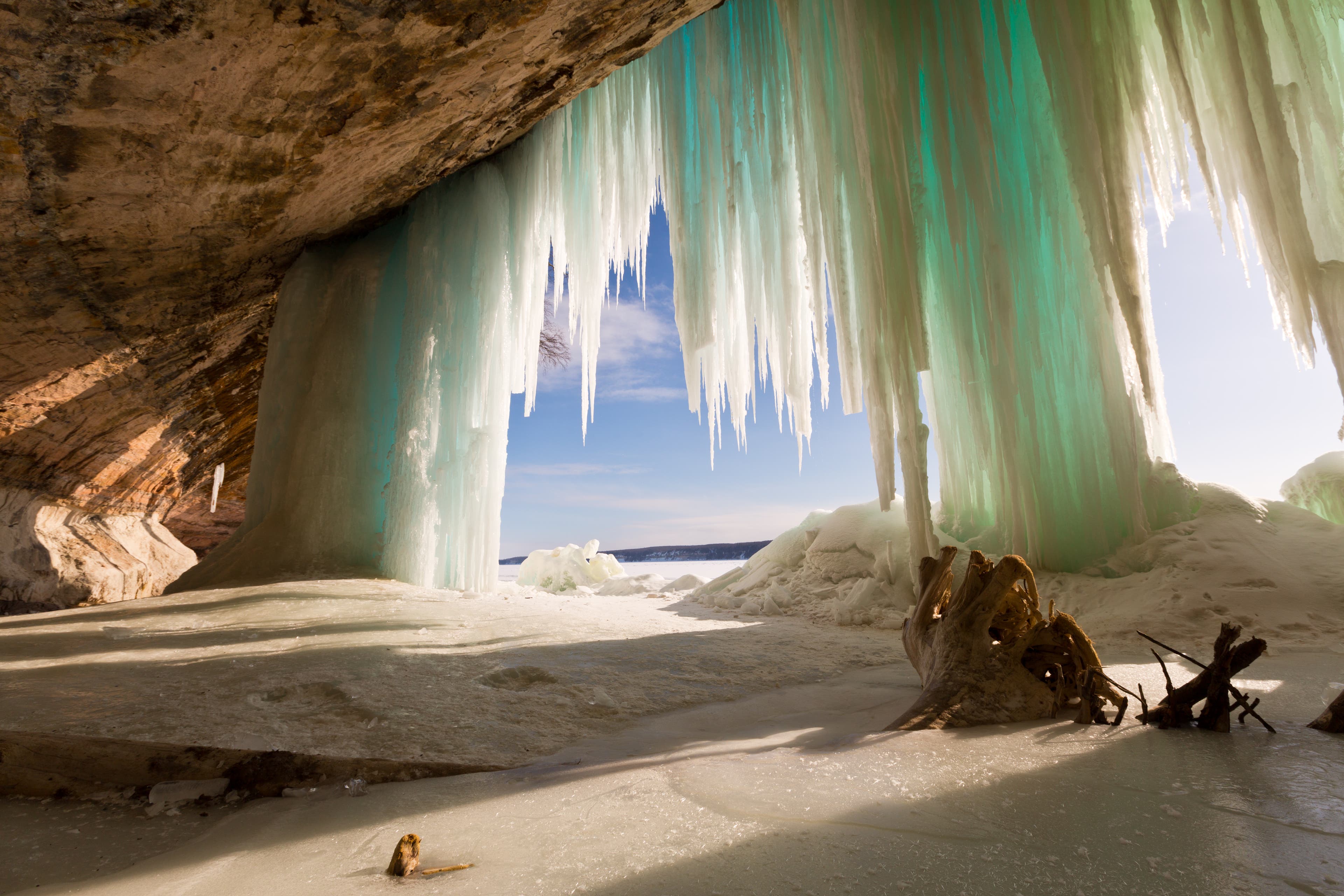 Icicles hang over the edge of a cave in Pictured Rocks Michigan. Photo is from the inside of the cave looking out as the sun shines through. A stump…